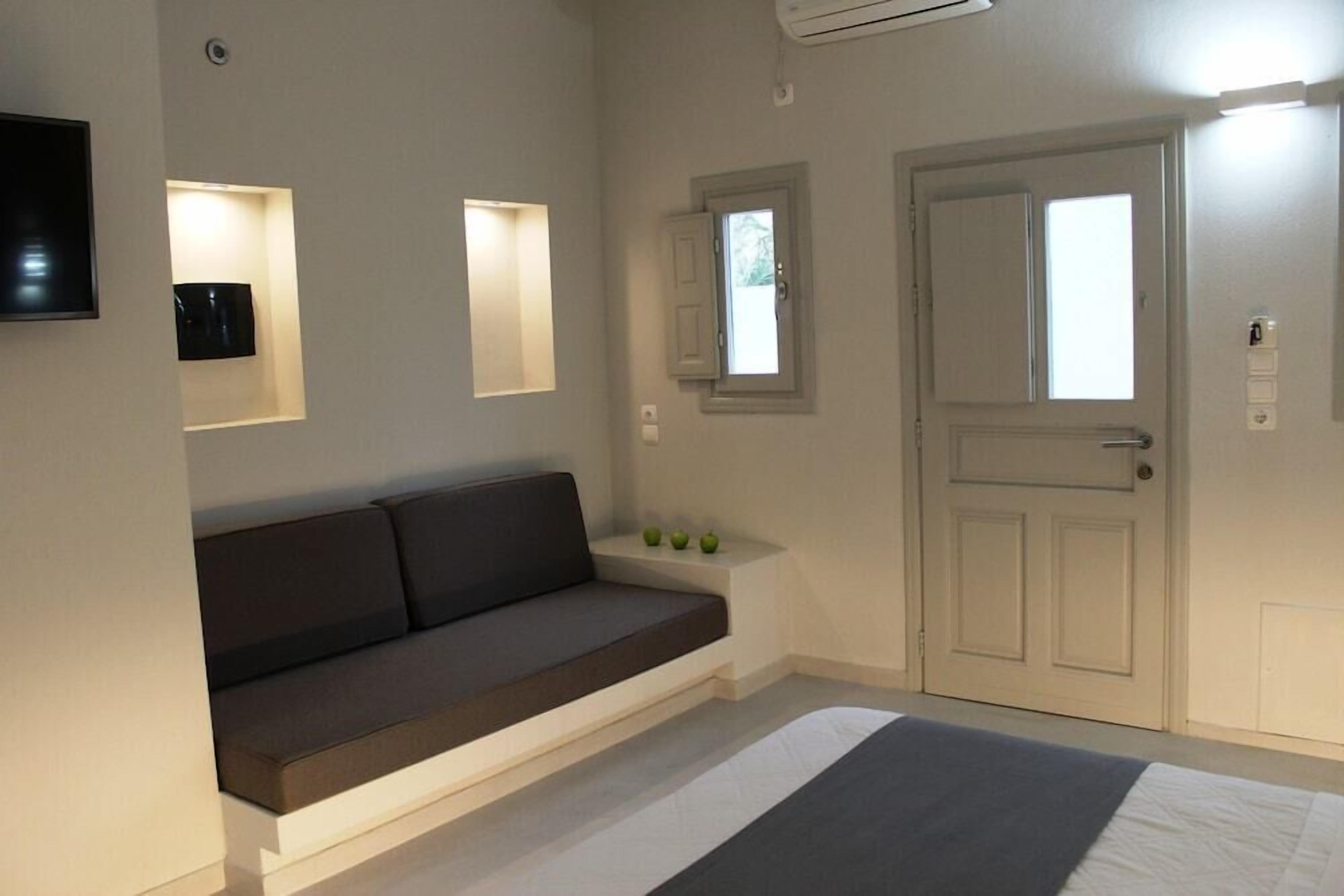Un dormitori modern amb un llit, un sofà, una televisió i una porta amb finestreta.
