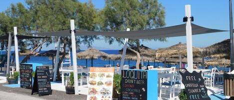 Een buitenterras met uitzicht op de zee, met borden voor Loquita waar bier van de tap, Corona, cocktails en gratis Wi-Fi worden aangeboden.