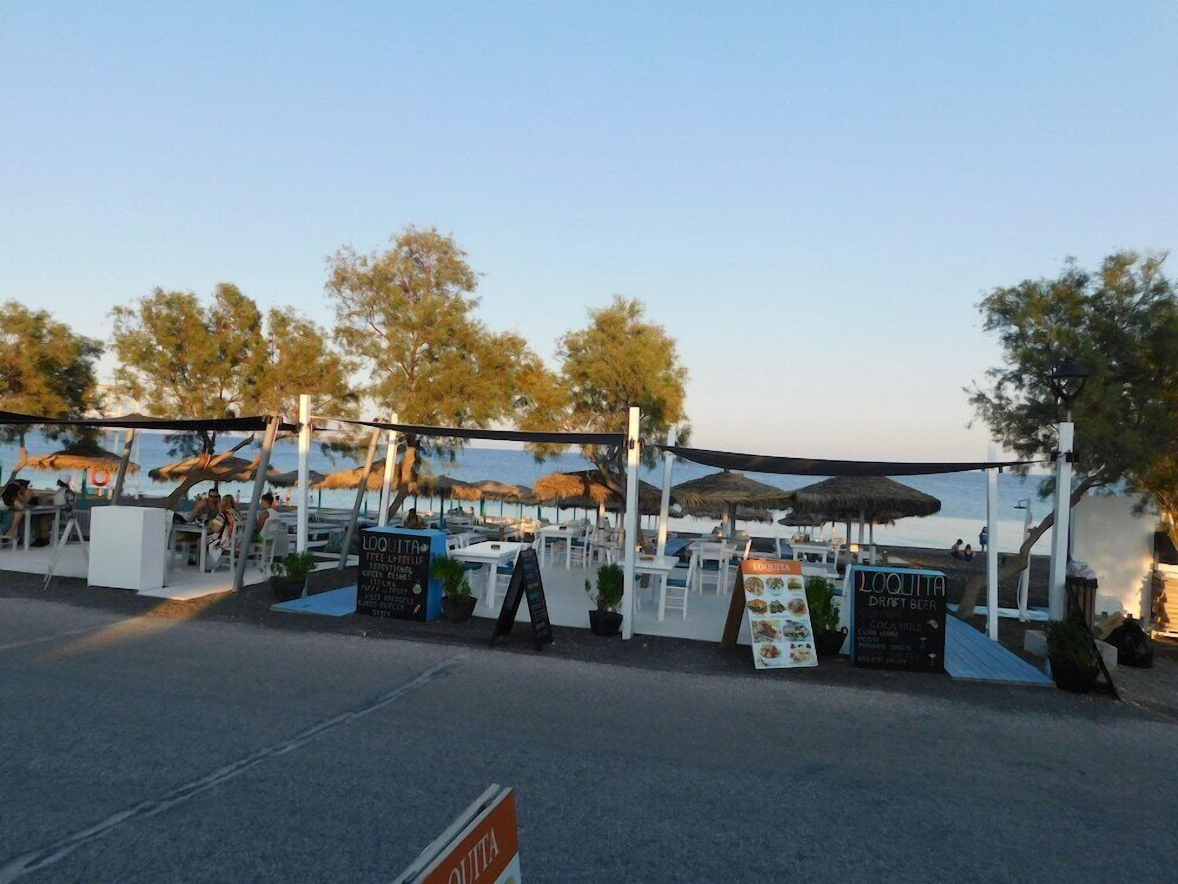 Un espace extérieur aménagé pour les repas, avec des tables et des parasols, entouré d’arbres et offrant une vue sur la mer.
