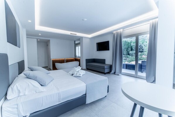 A modern hotel room with a large bed, a sofa, a TV, and a balcony with a view of greenery. - Lago BIN (Rocchetta Nervina)