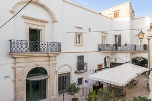 Un edificio blanco con varios balcones, una zona de estar al aire libre techada, y un cartel que indica un estacionamiento.