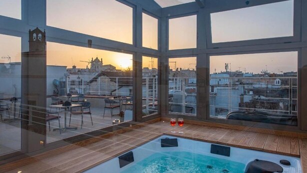 Une terrasse sur le toit dotée d’un jacuzzi, de murs en verre et offrant une vue sur le paysage urbain au coucher du soleil.