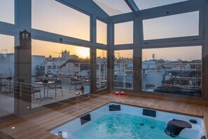 Eine Dachterrasse mit Whirlpool, Glaswänden und Blick auf die Skyline im Sonnenuntergang.