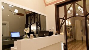 Een hotel receptie met een wit aanrecht, een computer, een bloemenvaas en een grote spiegel.