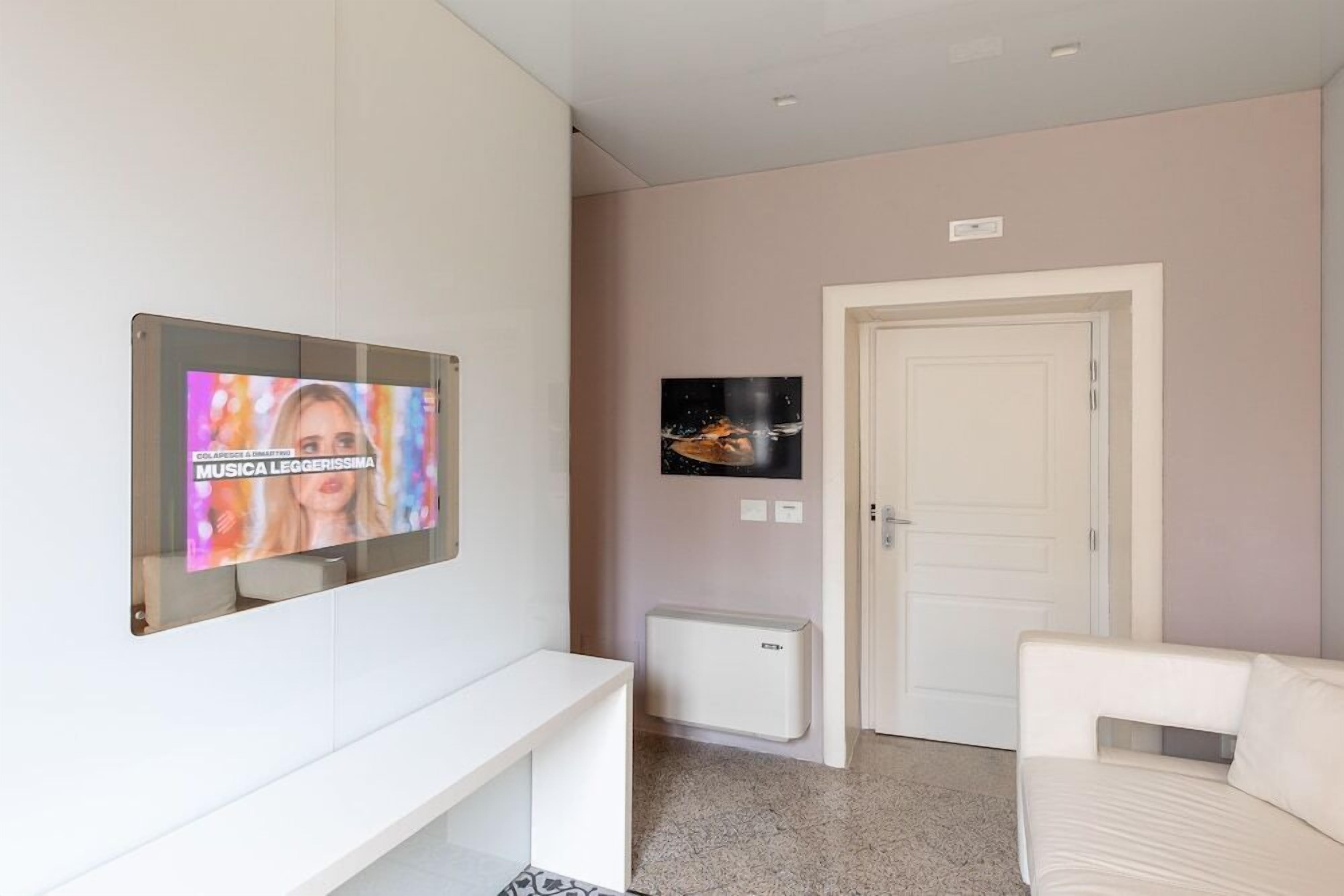 Een moderne woonkamer met een witte bank, een flatscreen televisie aan de muur en een witte deur.