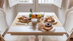 Une table à manger avec des aliments pour le petit-déjeuner, deux chaises blanches et une fenêtre donnant sur un balcon.