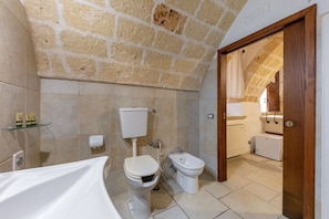 Une salle de bain avec un mur en pierre, des toilettes, un bidet et une baignoire.