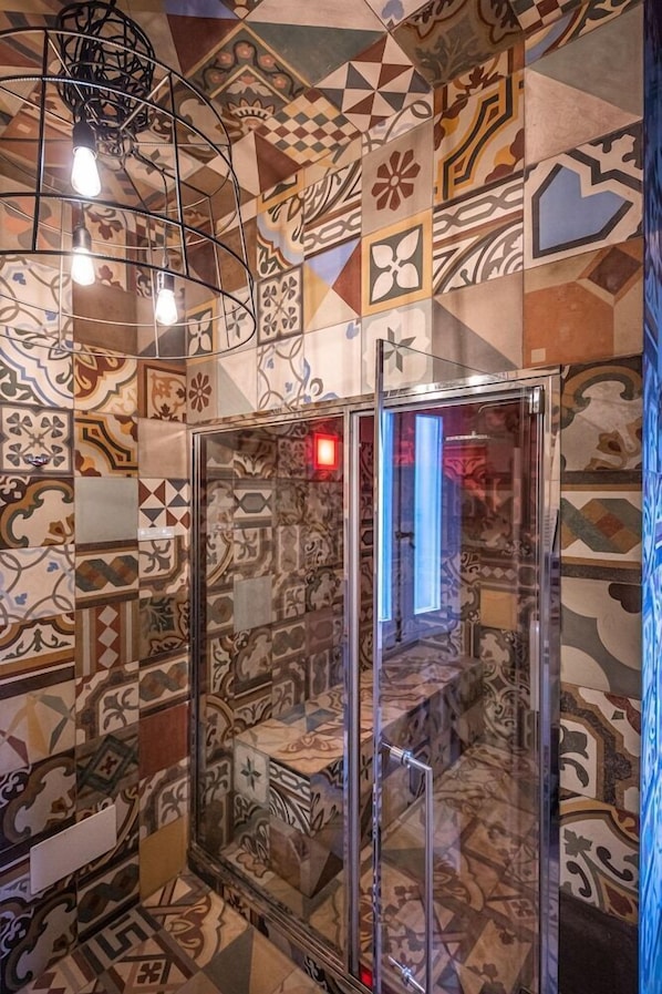 A bathroom with a shower enclosed in glass, surrounded by patterned tiles. - Palazzo Arco Cadura Hotel & Spa (Galatina)