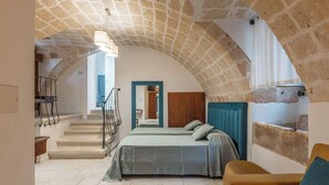 Une chambre avec un plafond en pierre, un lit, un canapé et un escalier menant à une autre pièce.