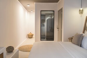 Een moderne slaapkamer met een groot bed, een glazen deur naar een badkamer en een klein rieten mandje op de vloer.