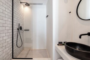 Un baño moderno con ducha de vidrio, un lavamanos negro y un espejo en la pared.