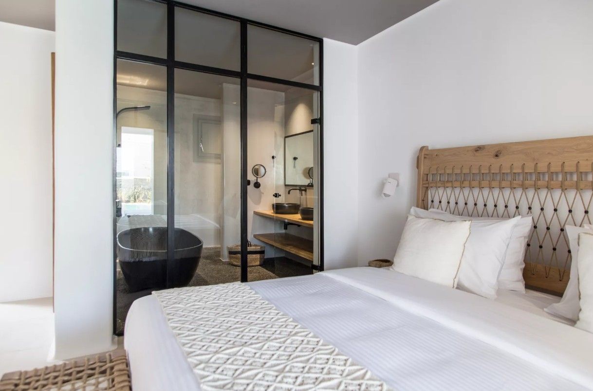 A modern bedroom with a large bed, a wooden headboard, a glass shower enclosure, and a visible bathroom.