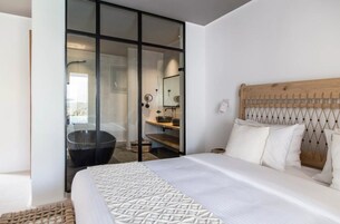 Un dormitorio moderno con una cama grande, un cabecero de madera, cabina de ducha de vidrio y baño a la vista.