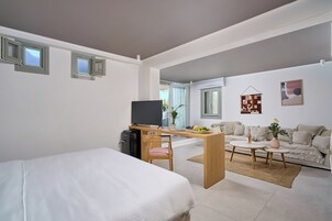 Habitación de hotel moderna con cama, escritorio, silla, televisor, sofá y una pequeña zona de comedor.