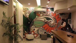 A reception area with a colorful mural, a reception desk, and a potted plant. - Front One Cabin Malioboro Jogja (Yogyakarta)