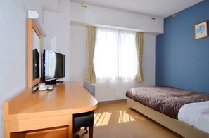 Ein Hotelzimmer mit einem hölzernen Schreibtisch, einem Fernseher, einem Bett mit einem gemusterten Überwurf und einem Fenster mit Vorhängen, sowie einer blauen Akzentwand.