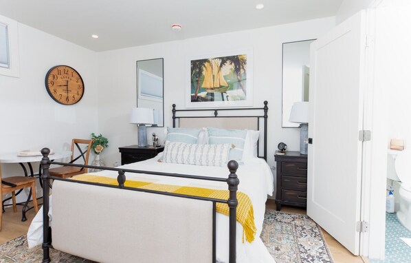 A bedroom with a bed, bedside tables, a clock, a painting, and a chair.