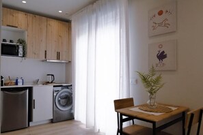 A compact kitchen with wooden cabinets, a washing machine, and a dining area with a table and chairs. - R&K Apartment Madrid - With private terrace in Madrid (Madrid)