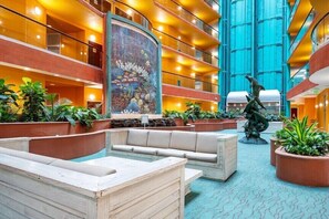 Eine Hotelhalle mit mehreren Etagen, einem großen Wandbild, Sitzbereichen und Topfpflanzen.