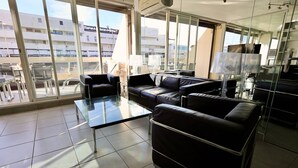 Ein modernes Wohnzimmer mit einem Glastisch, Ledersofas und Blick auf eine Stadtlandschaft durch große Fenster.