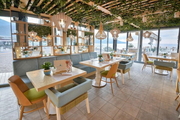 A restaurant with a terrace, wooden furniture, hanging lights, and a view of the sea. - Mediteran Wellness & Spa, Congress Center (Bečići)