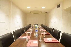 Un salón de conferencias con una larga mesa, sillas, botellas de agua, vasos y carpetas.