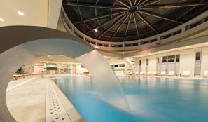 Una piscina interior con un diseño de techo moderno, sillones de descanso y una vista despejada del área de la piscina.