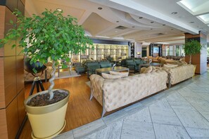 Un vestíbulo amplio con una gran planta en maceta, zonas de estar y un bar con estantes llenos de botellas.