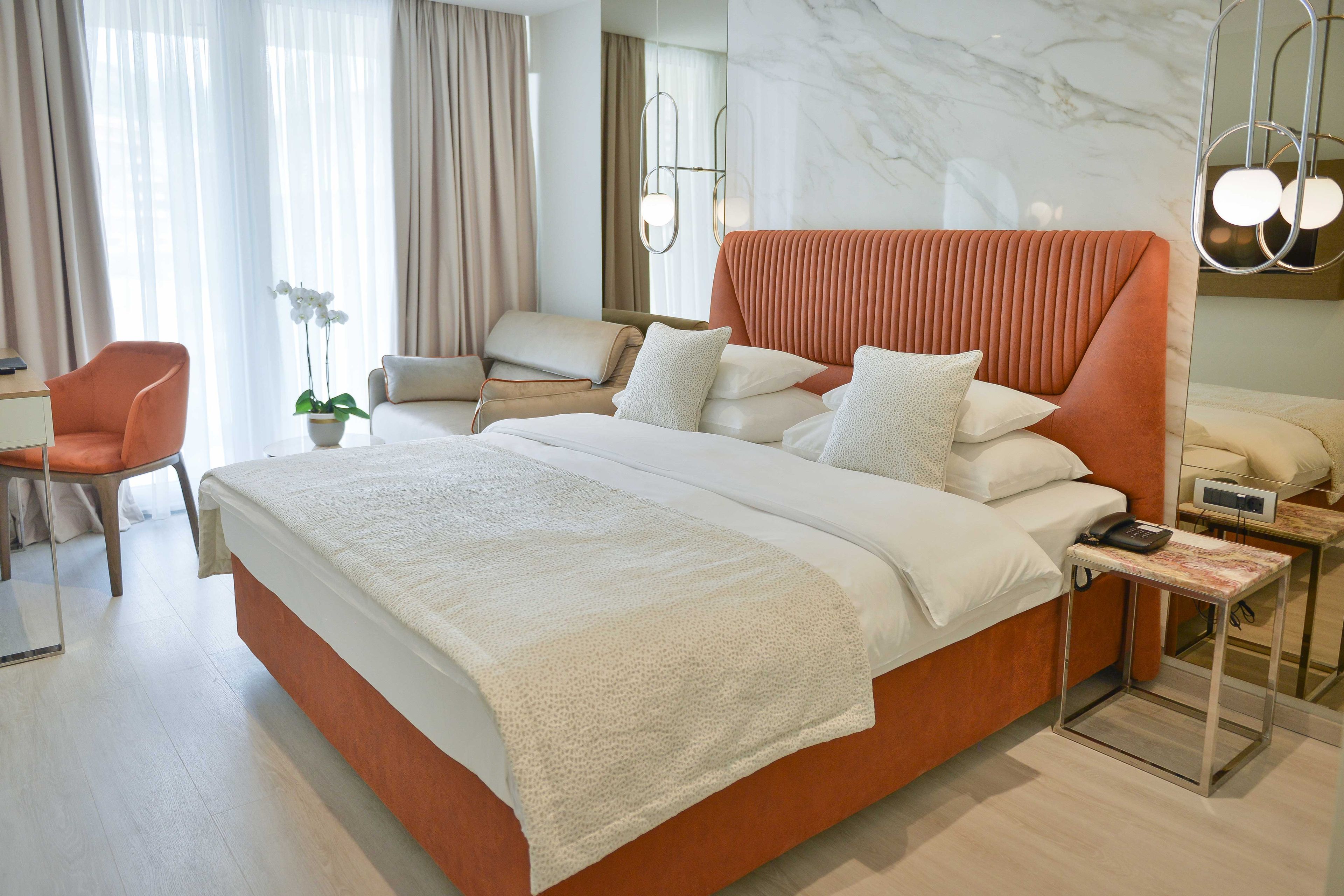 Una habitación de hotel moderna con una cama grande, una mesita de noche con teléfono, una silla, un escritorio y una planta en maceta.