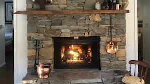 A stone fireplace with a framed picture above, a shelf with decorative items, and a chair in front. - Lakefront Event Venue: Wedding -Reunions -Retreats (Cedar Mountain)