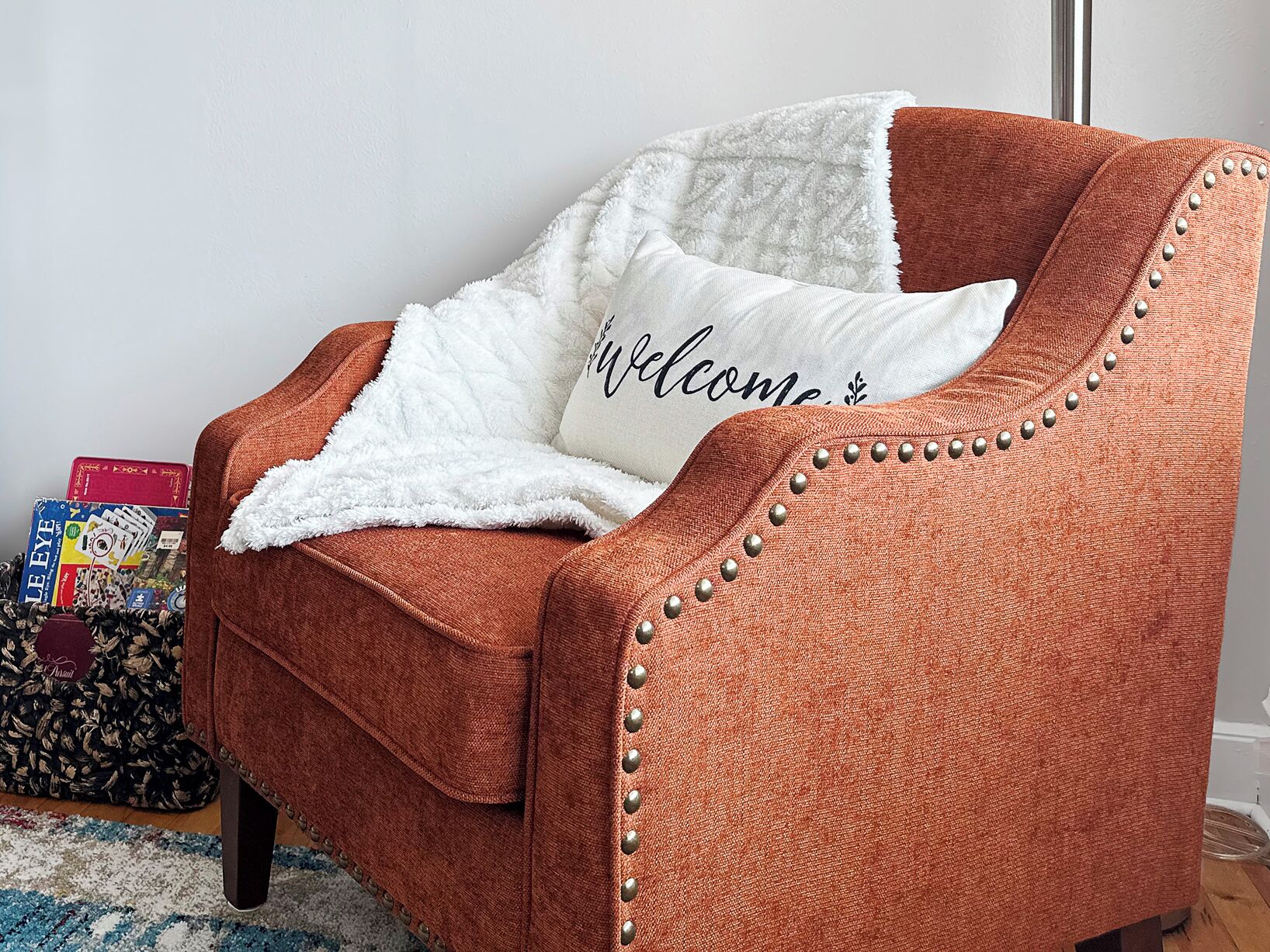 Un sillón marrón con un plaid blanco y un cojín con el texto 'Welcome'.