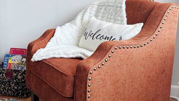 Un sillón marrón con un plaid blanco y un cojín con el texto 'Welcome'.