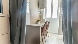 A modern kitchen with a white countertop, two pink chairs, and a wall-mounted light fixture. - Old Town Rooms Ljiljana (Pula)