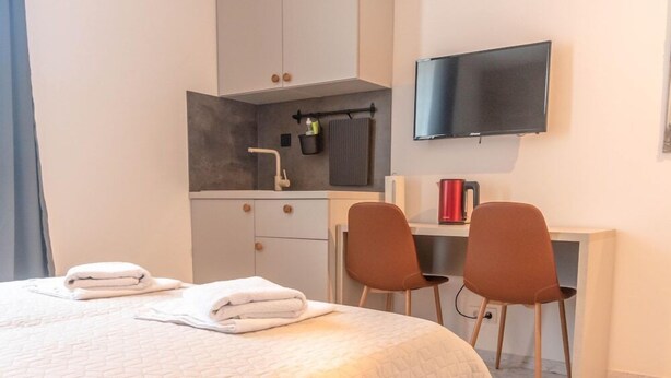 A hotel room with a bed, two chairs, a desk, a TV, and a kitchenette. - Old Town Rooms Ljiljana (Pula)