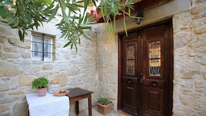 Un edificio de piedra con una puerta de madera, una pequeña mesa con mantel blanco y plantas en macetas.