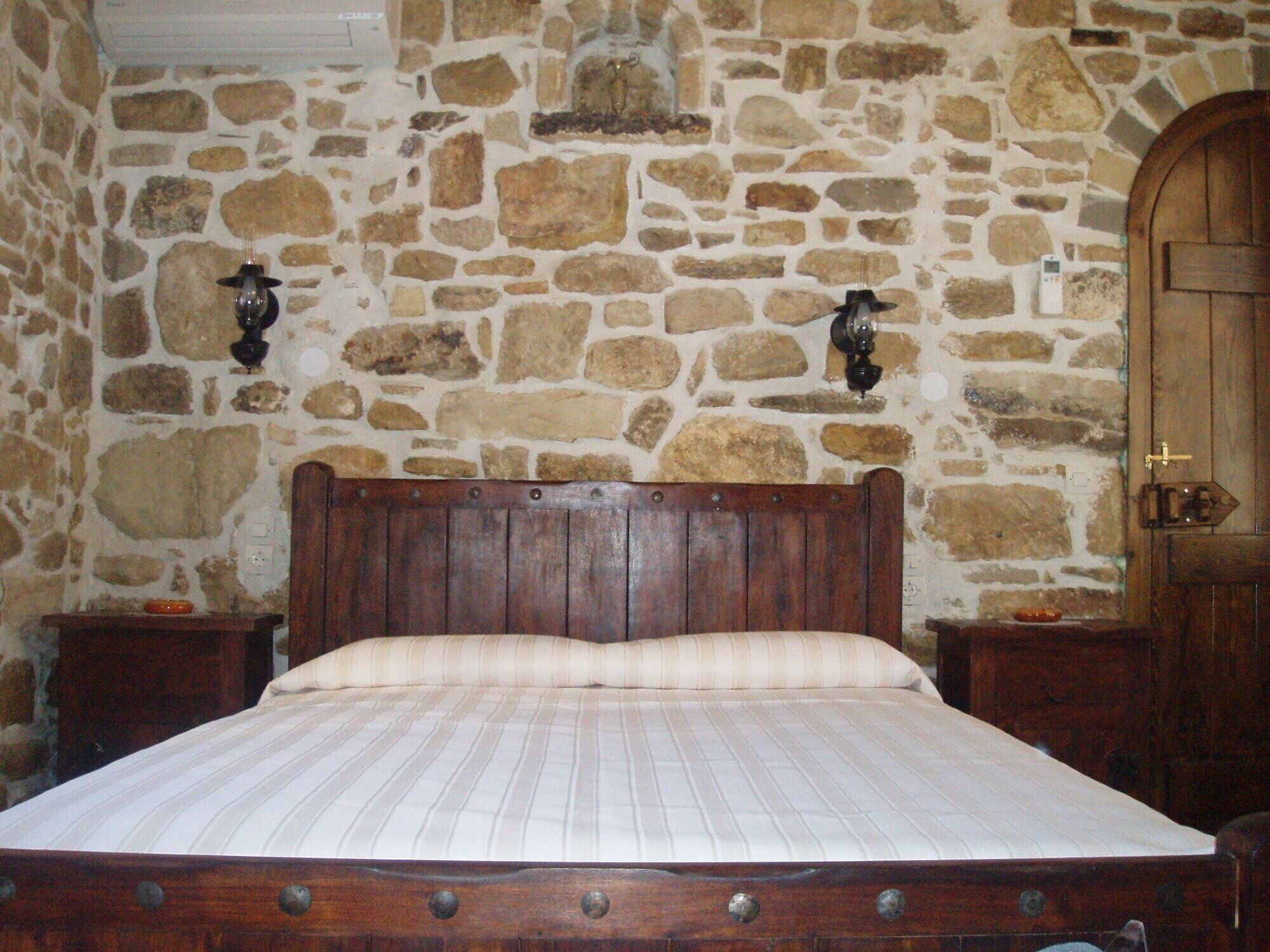 A bedroom with a stone wall, a wooden bed frame, two nightstands, and a wooden door.