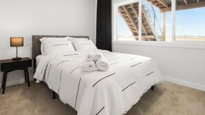 A neatly made bed with white bedding and rolled towels, a bedside lamp, and a window with a view of a wooden staircase and a clear sky. - Modern 2 BR walkout suite|5 mins to Airport
Entire guest suite in Calgary,Canada (Calgary)