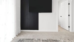A modern room with a large flat-screen TV mounted on a dark wall, a white door, and a patterned rug on the floor. - Modern 2 BR walkout suite|5 mins to Airport
Entire guest suite in Calgary,Canada (Calgary)