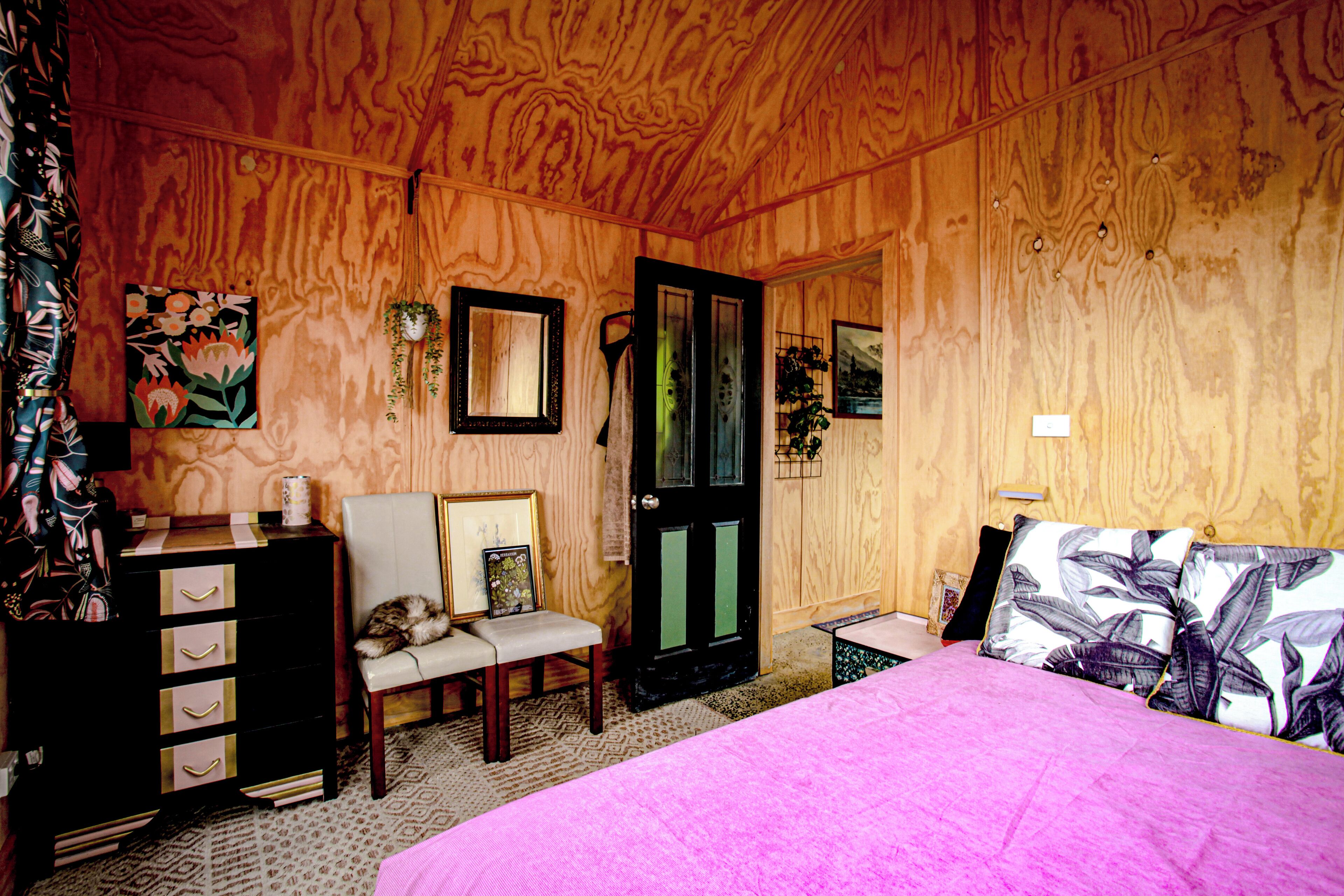 A wooden-paneled room with a bed, a chair, a dresser, and a door.
