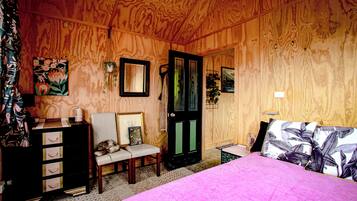 A wooden-paneled room with a bed, a chair, a dresser, and a door.