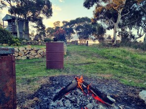 A rustic outdoor setting with a fire pit, a wooden structure, and a stone wall.