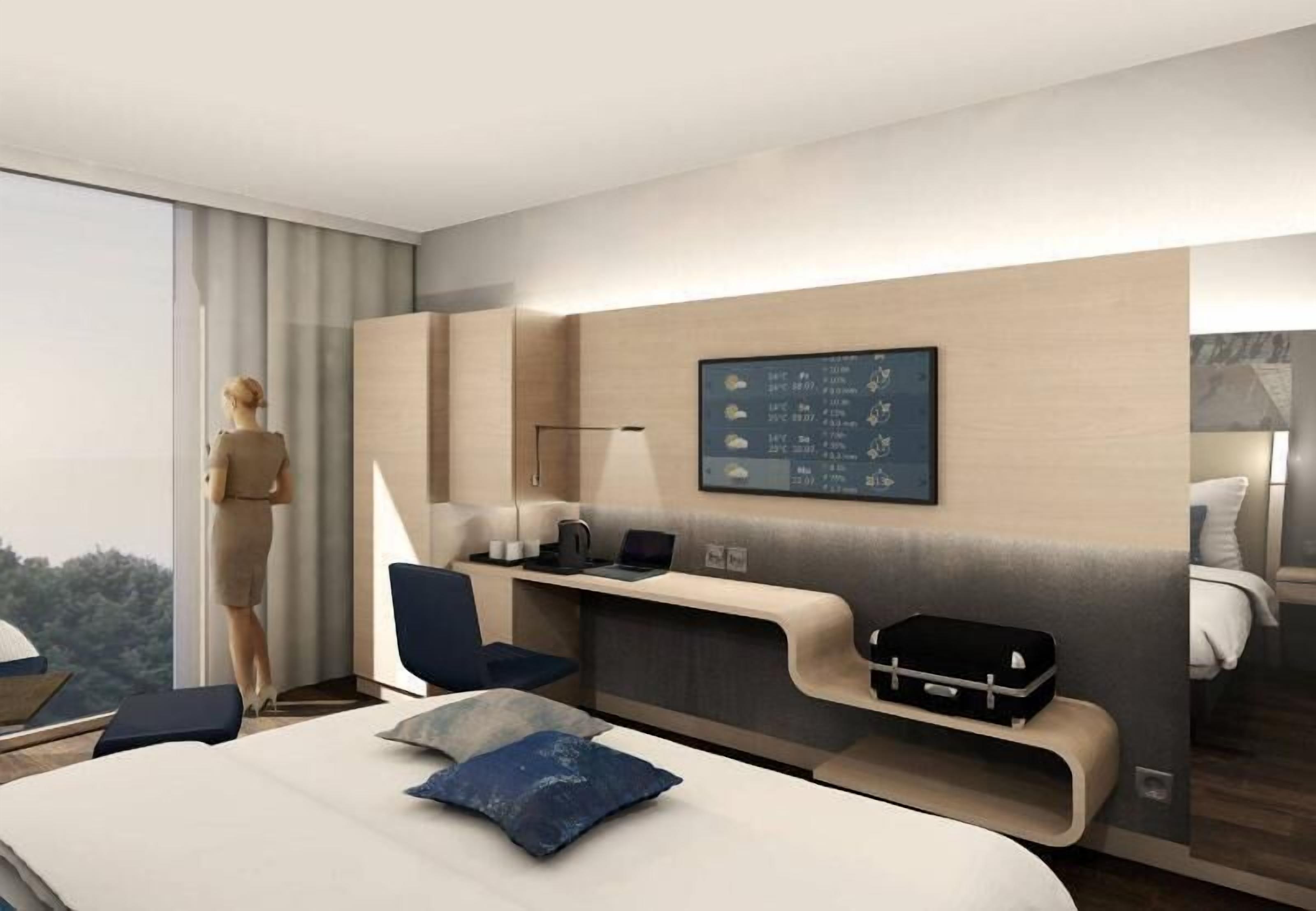 A modern hotel room with a bed, a desk, a laptop, a chair, and a large window offering a view of the outdoors.