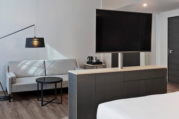 A modern hotel room with a sofa, a small round table, a TV mounted on a cabinet, and a bed. - Courtyard Munich Garching (Garching)