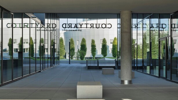 A modern building with the name 'COURTYARD' on the facade, large glass windows, and a central column.
