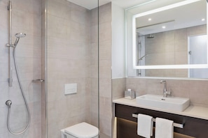 A modern bathroom with a glass-enclosed shower, a white toilet, a sink with a mirror above it, and a towel rack. - Courtyard Munich Garching (Garching)
