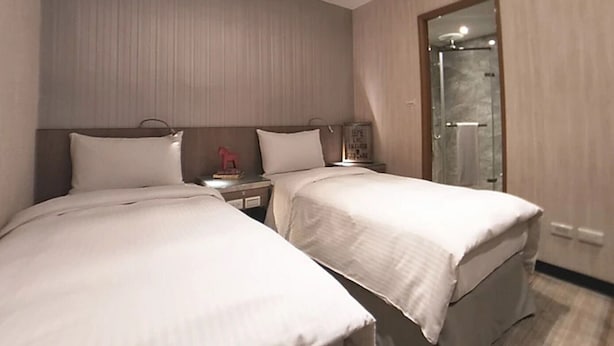 Habitación de hotel con dos camas, una mesita de noche, un espejo y zona de ducha.