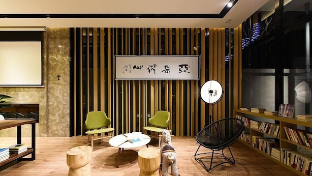A modern interior with a wooden floor, green chairs, a round table, a black chair, and a bookshelf. - Atour Hotel (Hangzhou)