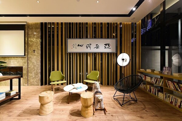 A modern interior with a wooden floor, green chairs, a round table, a black chair, and a bookshelf. - Atour Hotel (Hangzhou)