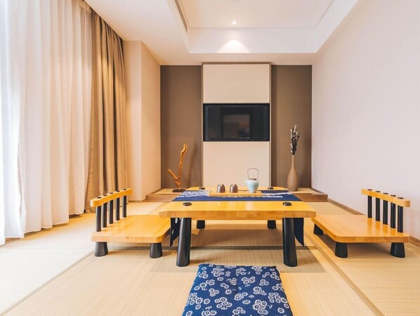 A modern living room with a central wooden table, a sofa, and a TV mounted on the wall. - Atour Hotel (Hangzhou)