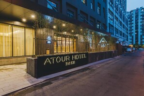 La façade d’un hôtel, avec une enseigne indiquant « ATOUR HOTEL », présente un design architectural moderne caractérisé par des lignes verticales et un balcon.